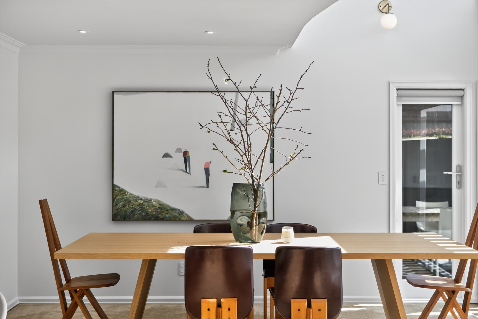 Timber dining table styled with sculptural branches, artwork and warm leather chairs