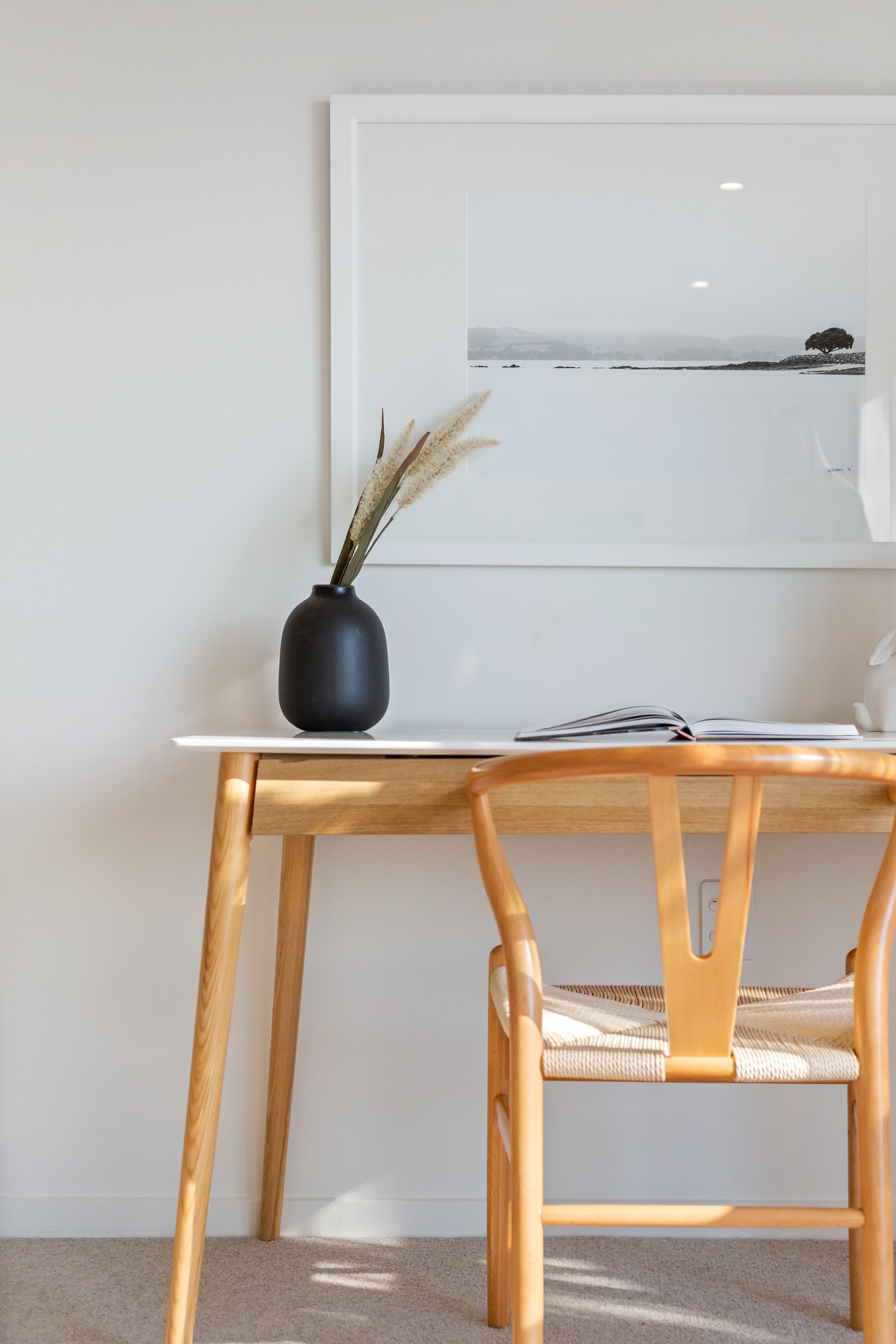 Sunlit desk styled with timber furniture, monochrome artwork and a sculptural vase