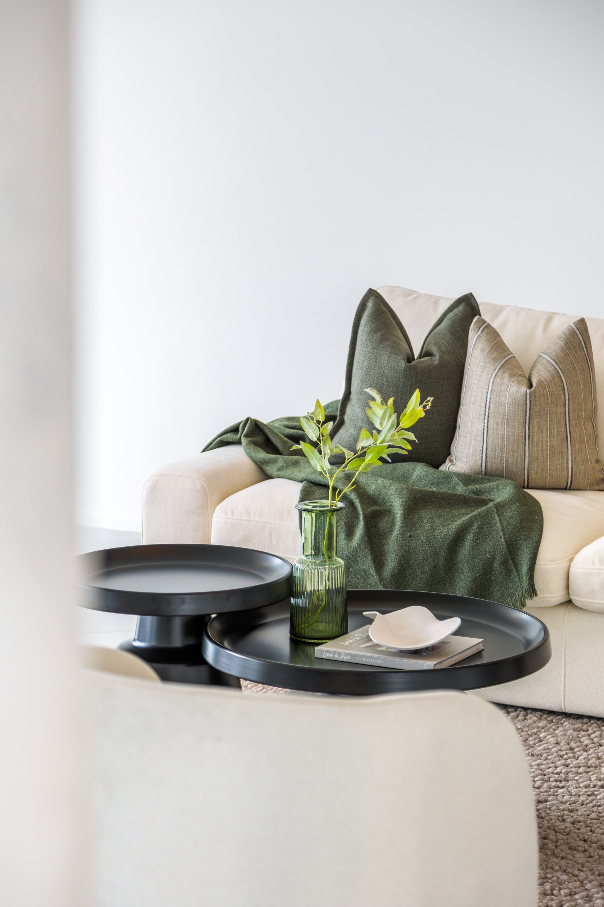 Layered living room detail with a green throw, neutral cushions and black nesting tables