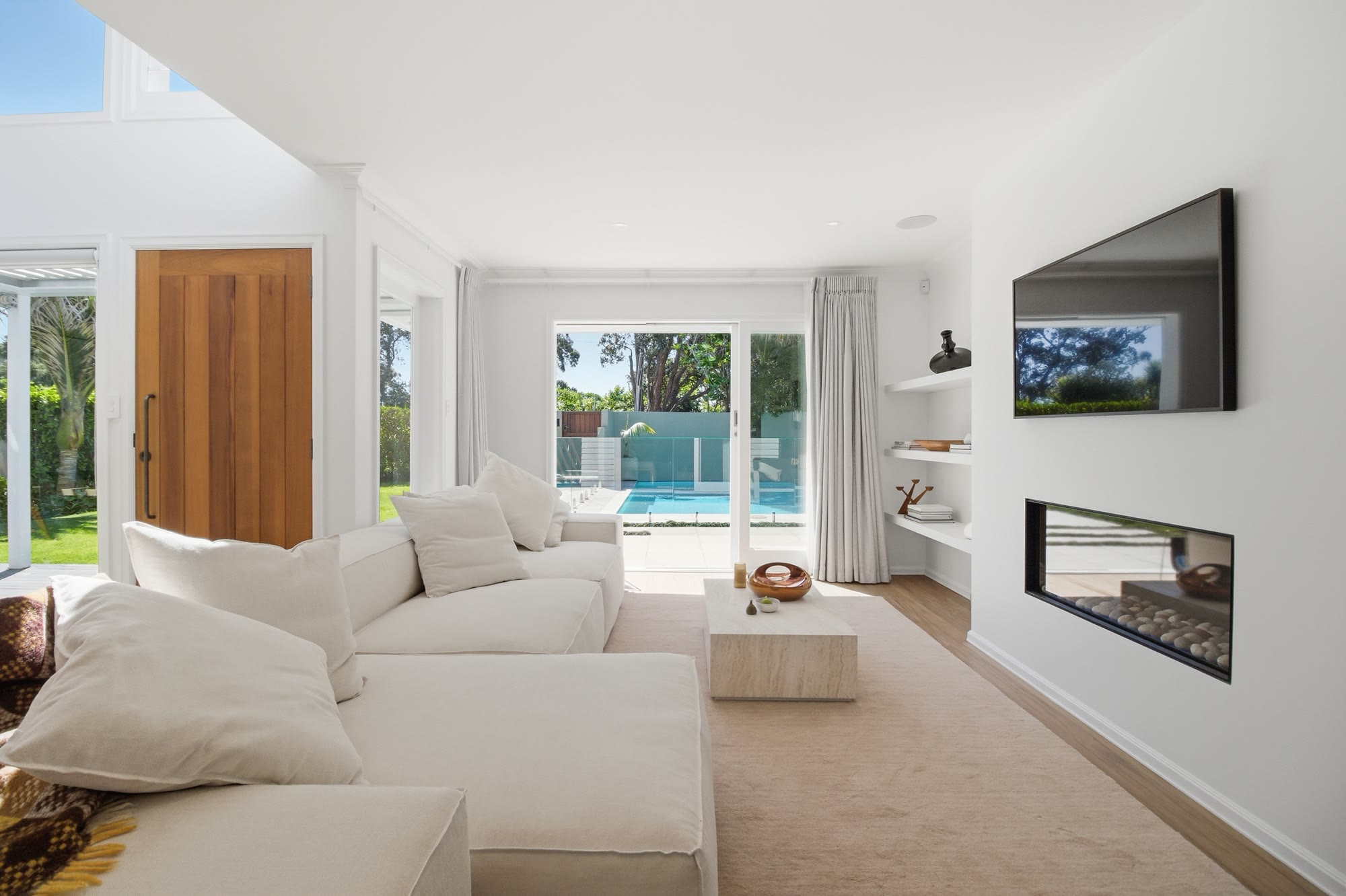 Complete living and dining scheme with neutral furniture, timber accents and a bright kitchen beyond