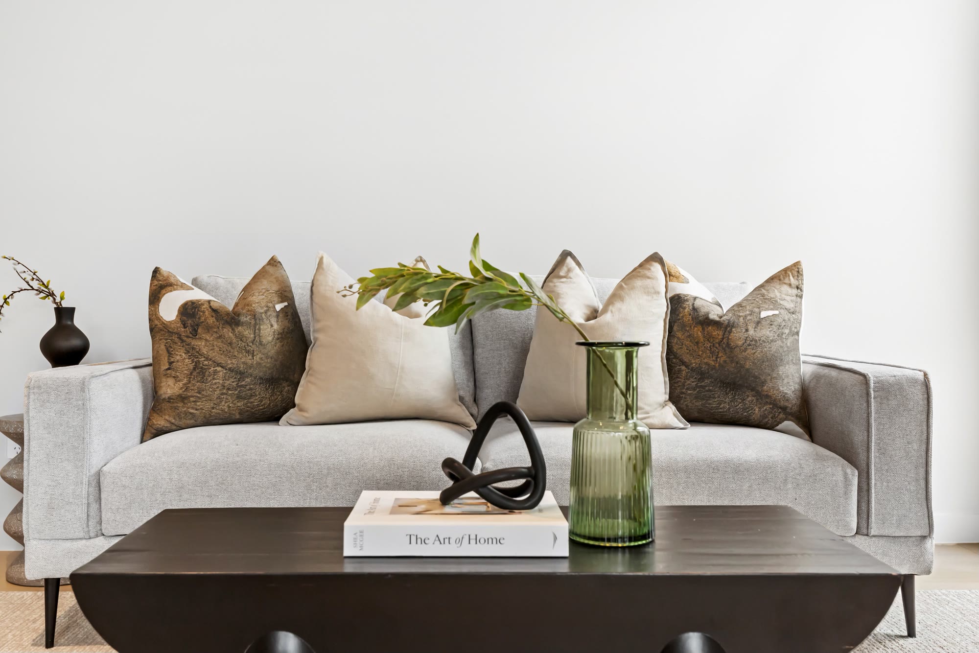 Neutral sofa layered with cushions, greenery and a dark coffee table