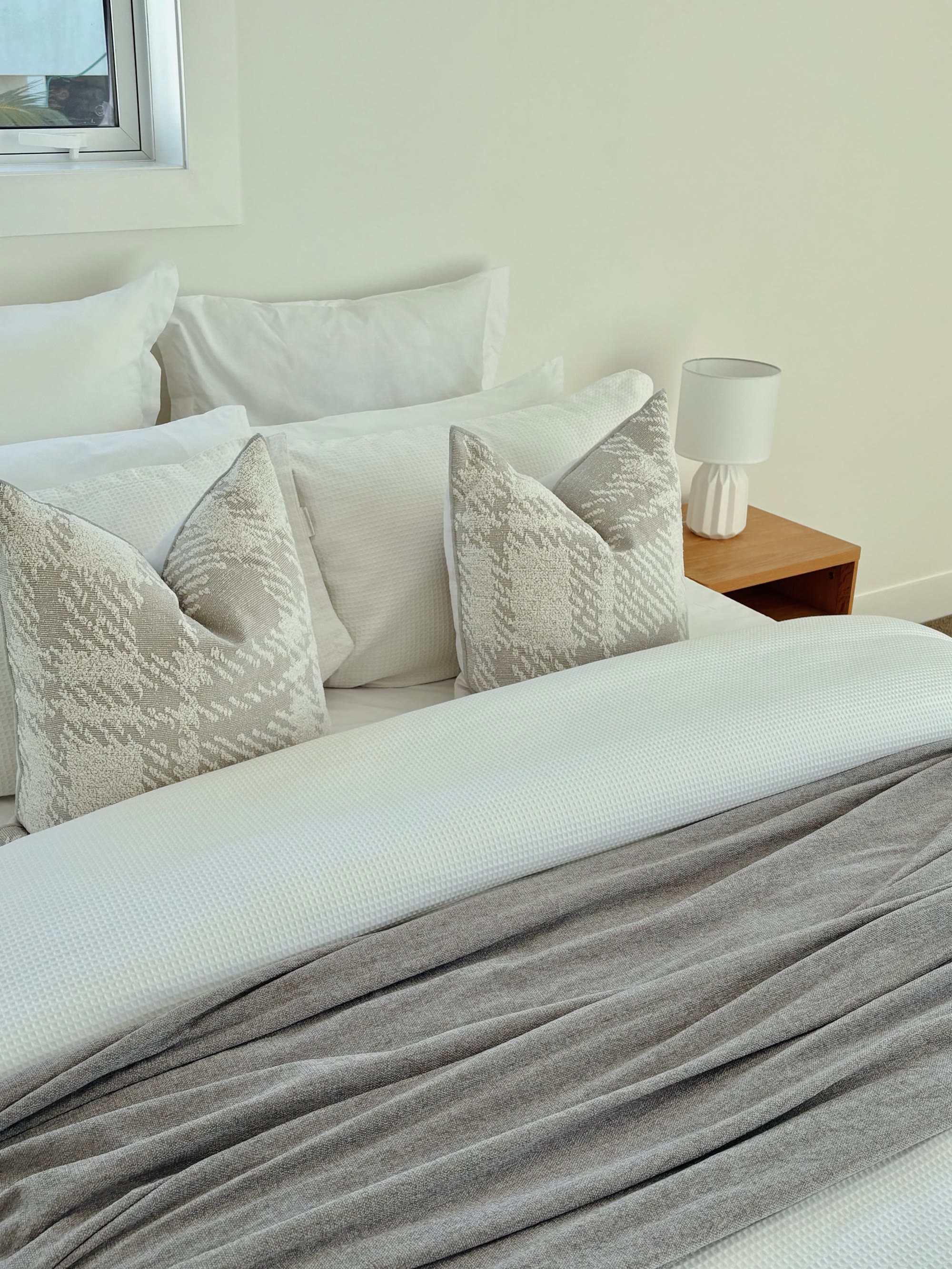 Bedroom detail with layered white bedding, soft grey cushions and a timber bedside table