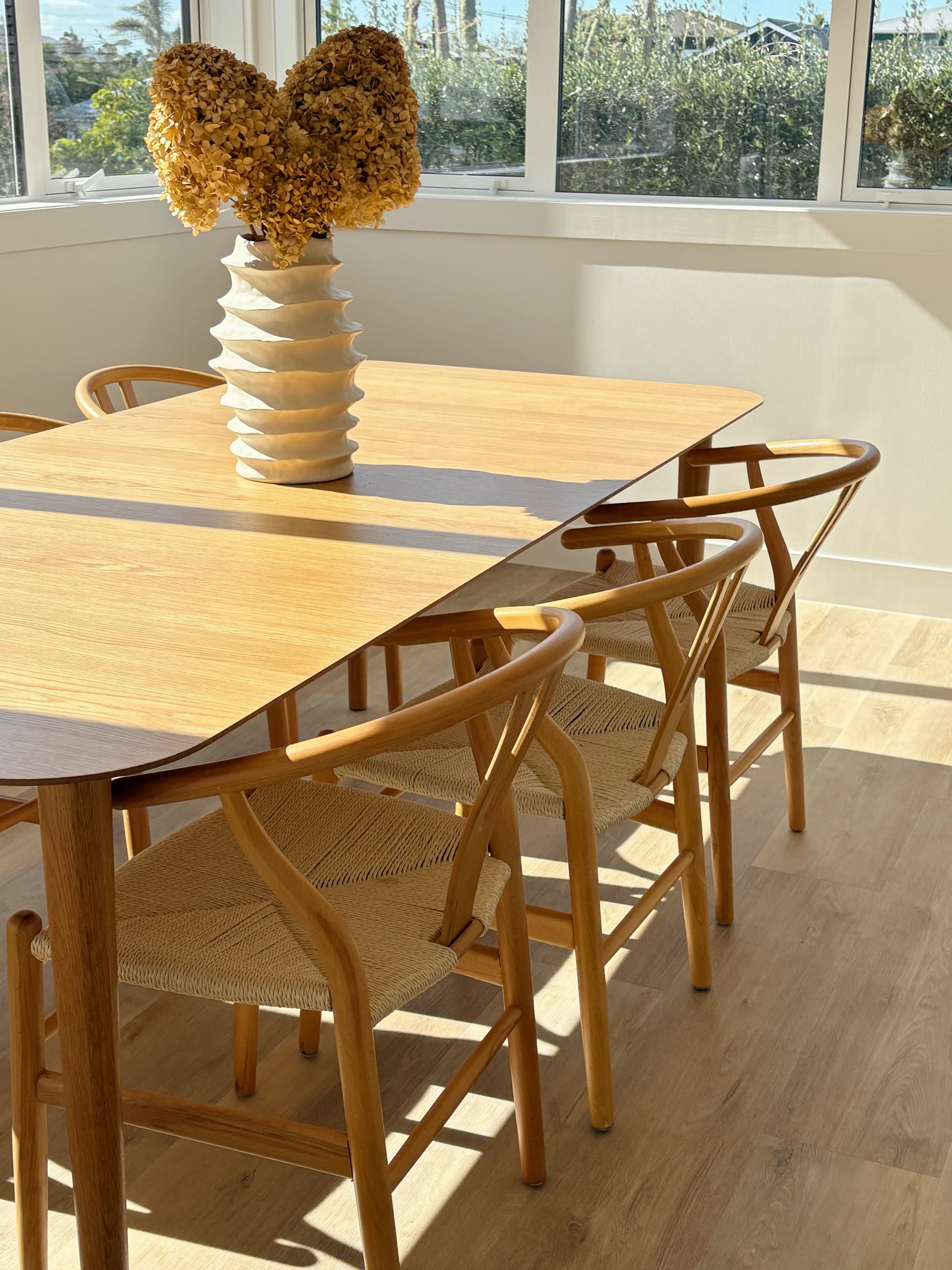 Sunlit oak dining table styled with woven timber chairs and a sculptural floral arrangement