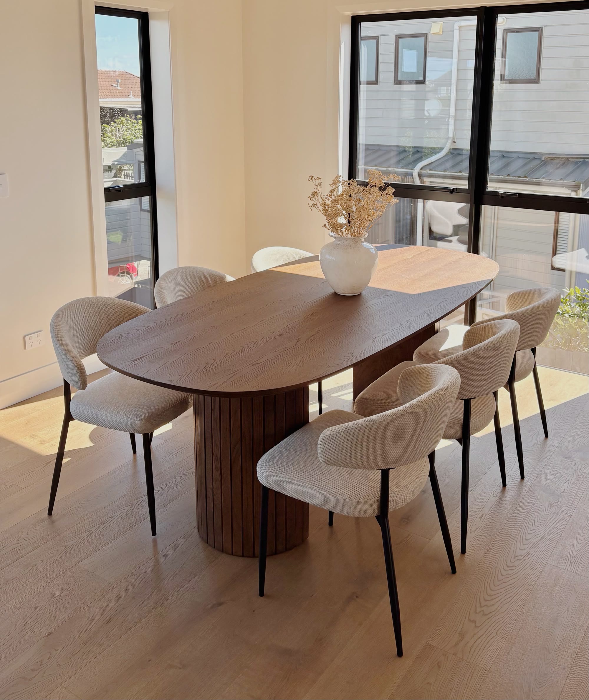 Walnut dining table surrounded by upholstered chairs in a bright window-lined room