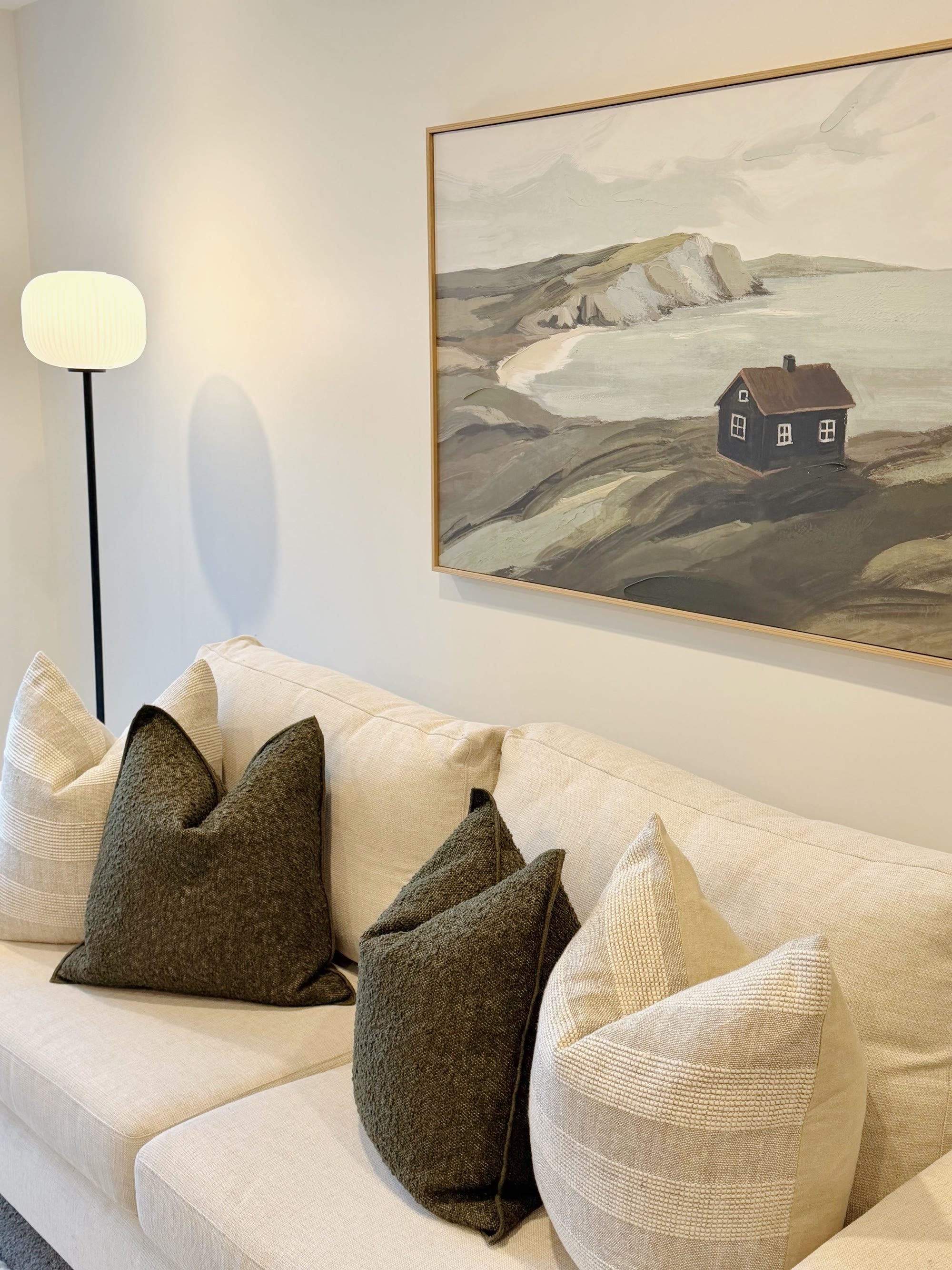 Cream lounge seating with charcoal cushions beneath large coastal artwork