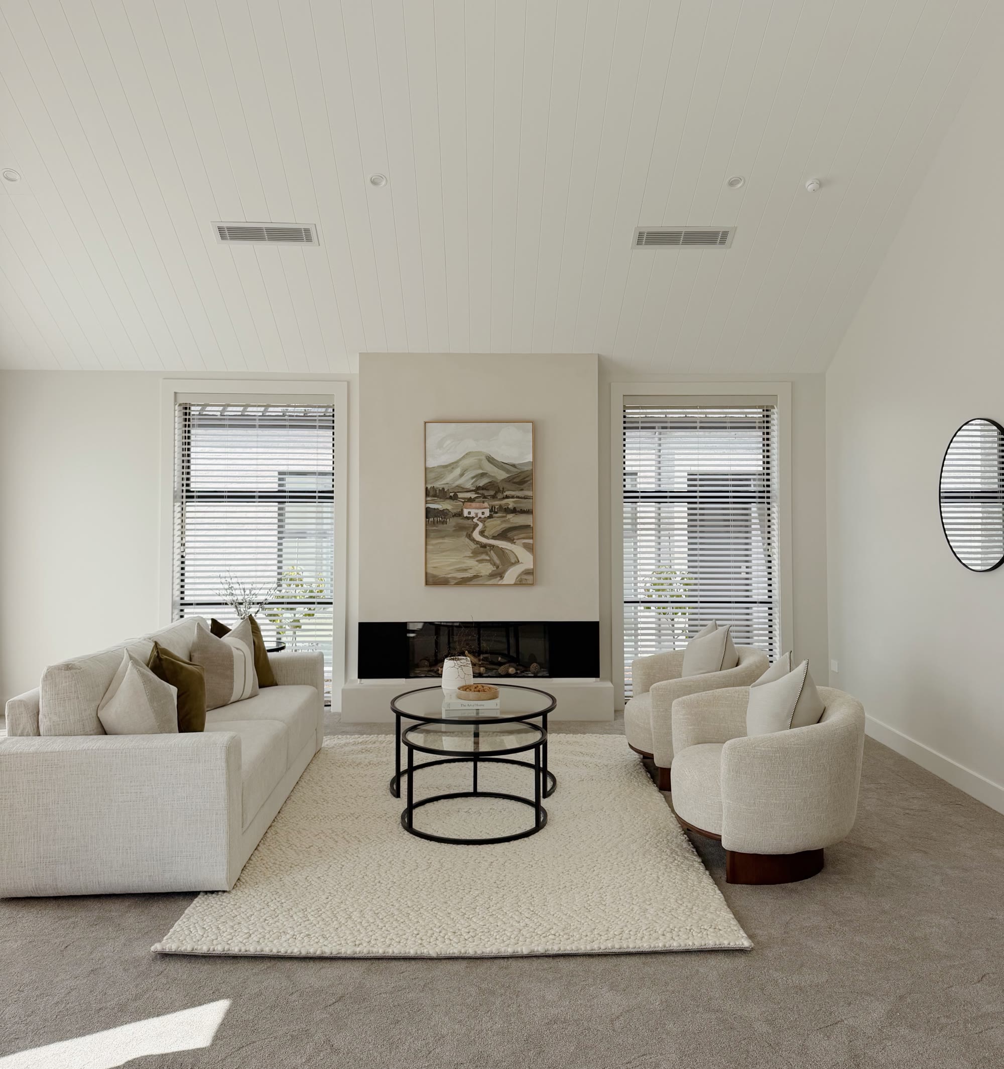 Cream sofa and rounded armchairs arranged around glass nesting tables in a bright lounge with a fireplace