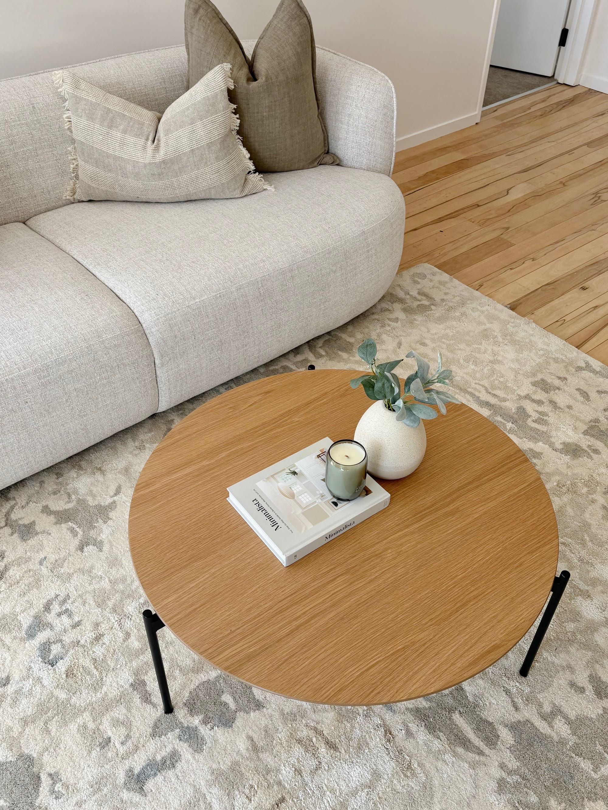 Neutral lounge with a curved sofa, pale patterned rug and round oak coffee table