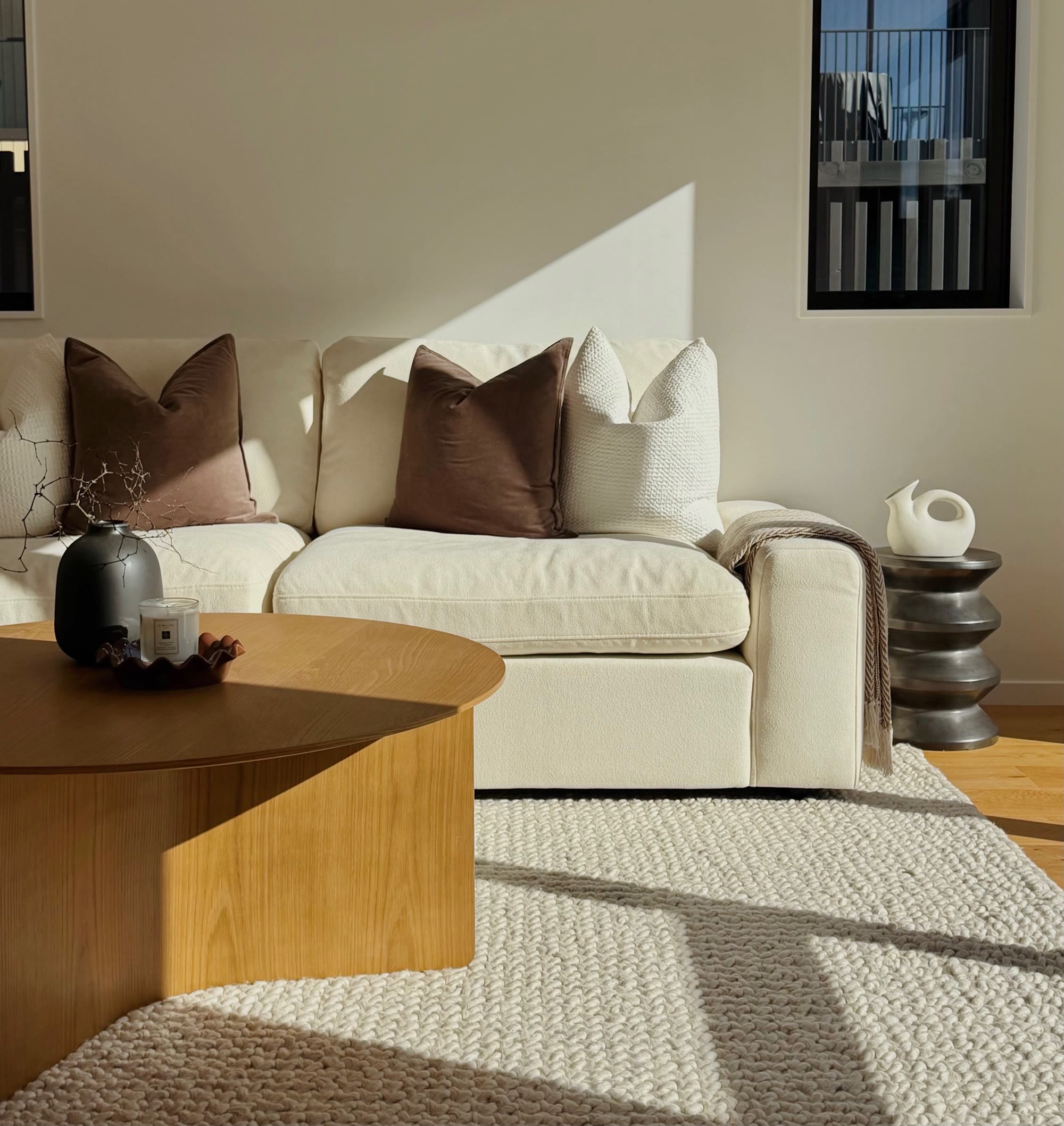 Sunlit cream sofa styled with chocolate cushions beside a sculptural side table