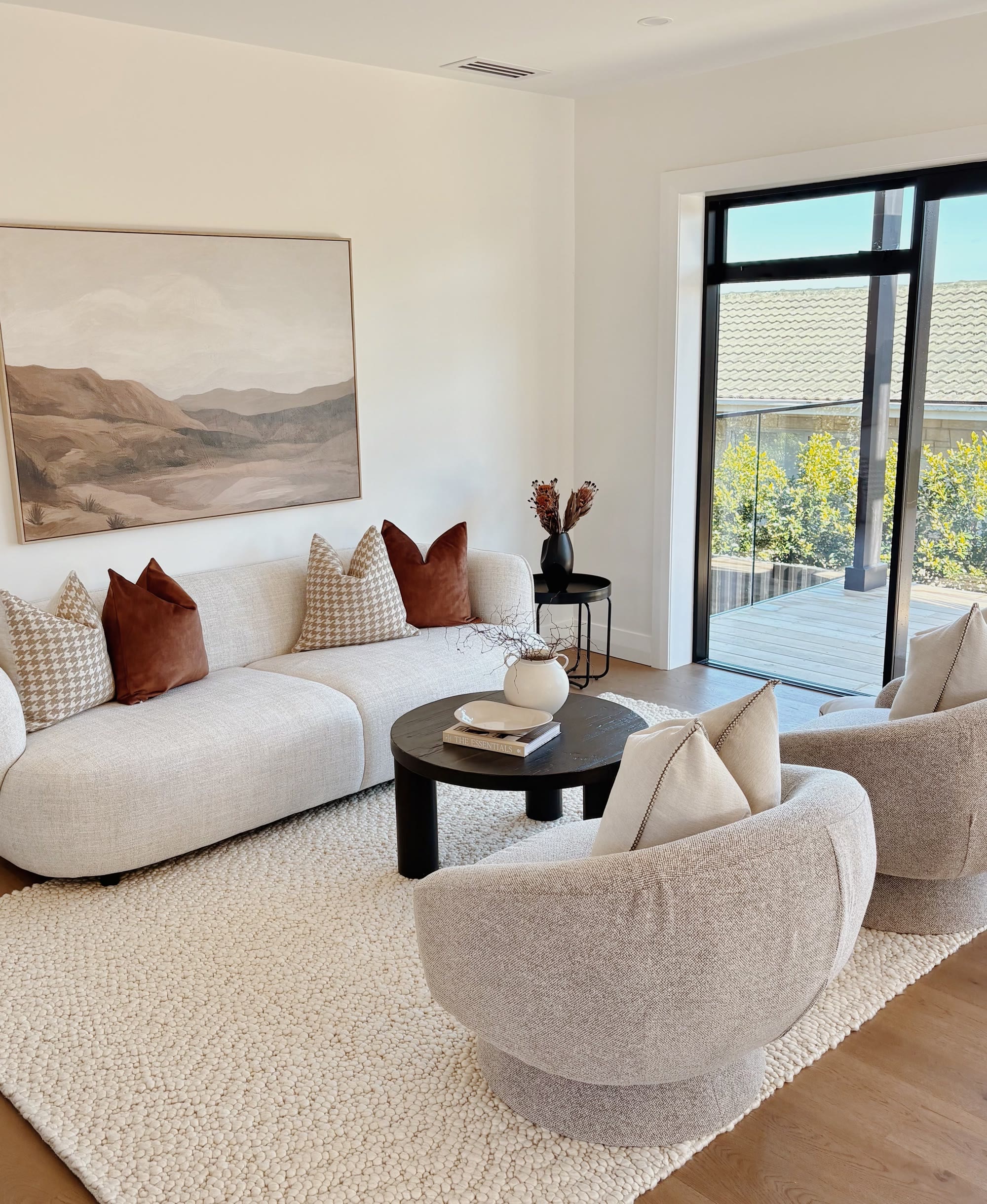 Warm neutral lounge styled with a curved sofa, two occasional chairs and terracotta cushions