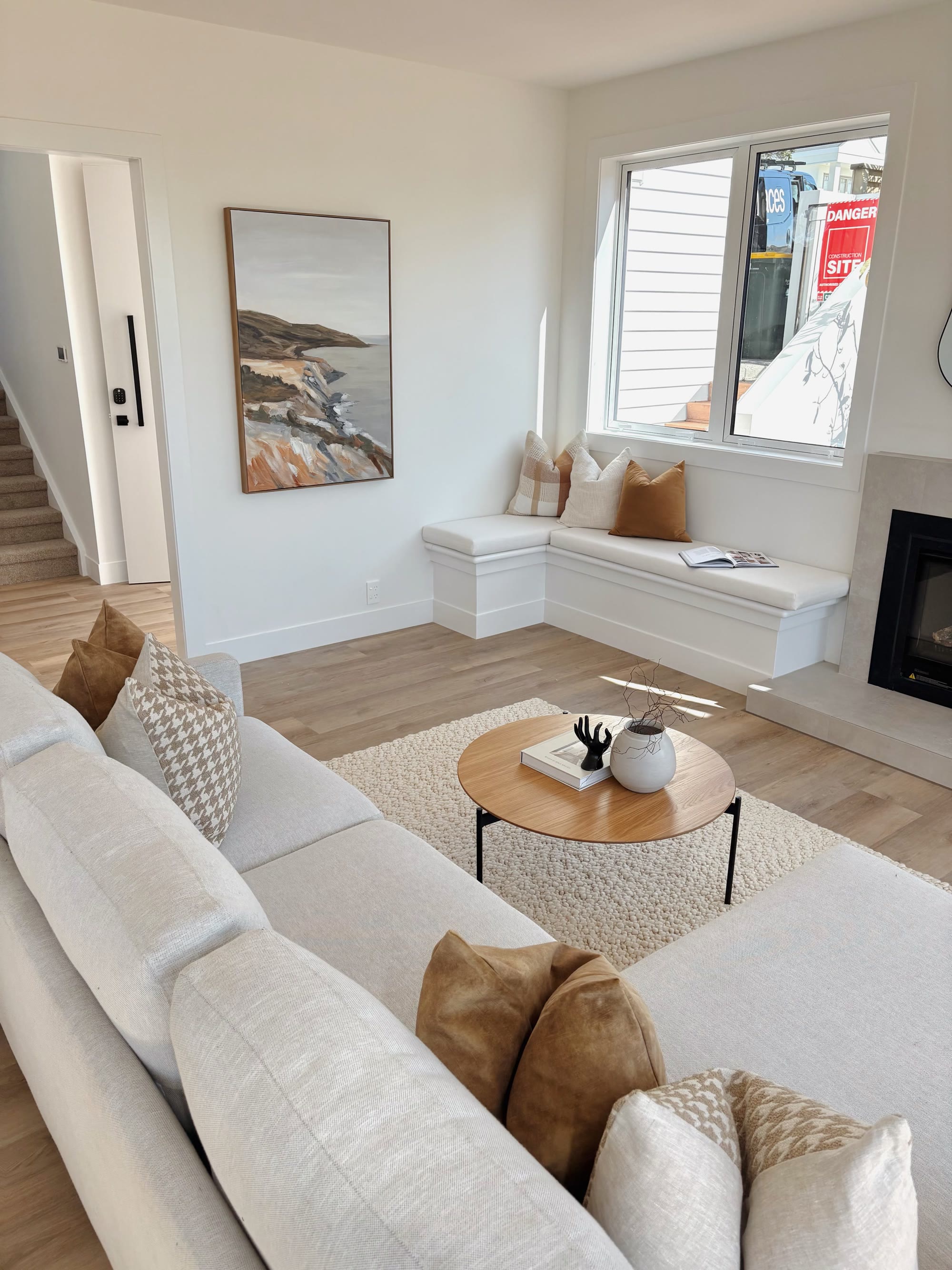 Bright lounge with a cream sectional, window seat, round coffee table and warm neutral cushions