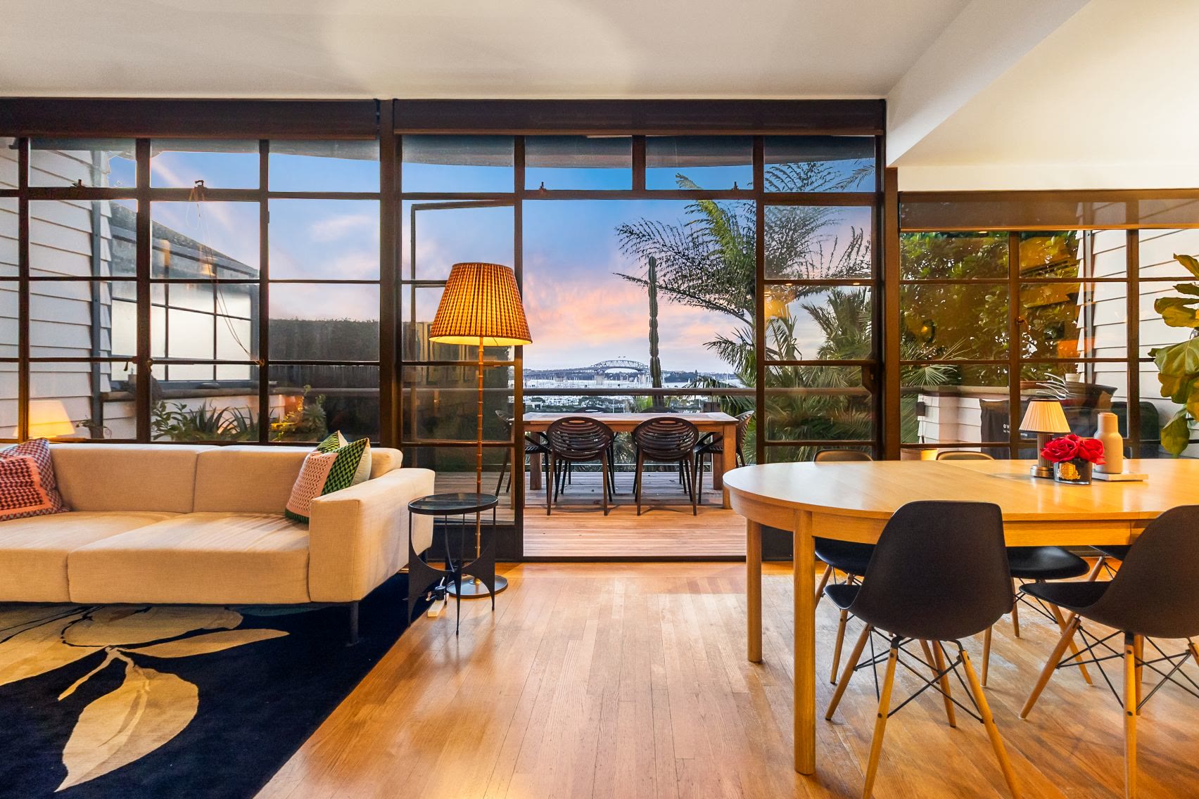 Harbour-facing Auckland living and dining room framed by steel windows at sunset