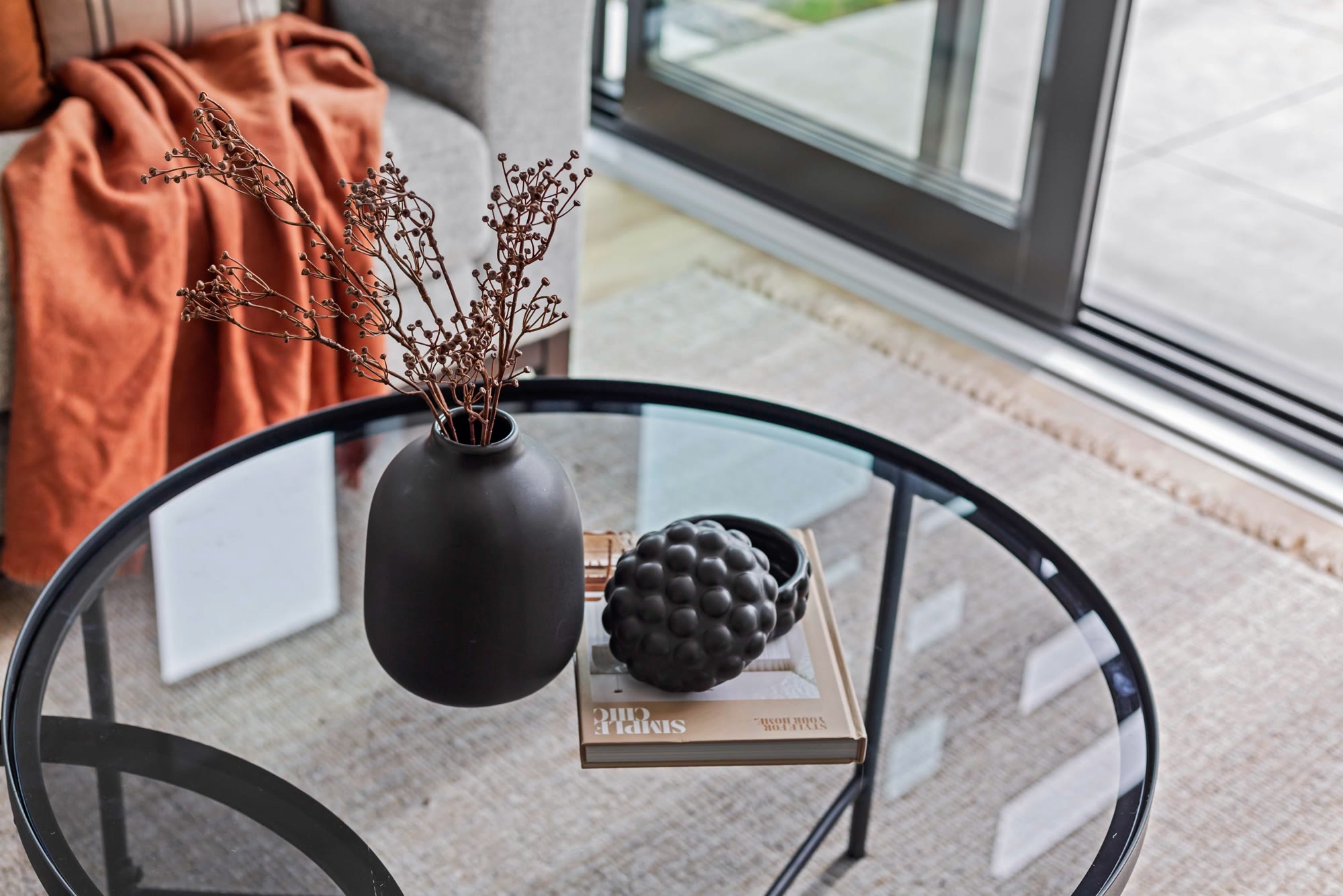 Coffee table styled with sculptural black ceramics, dried foliage and a rust-toned throw